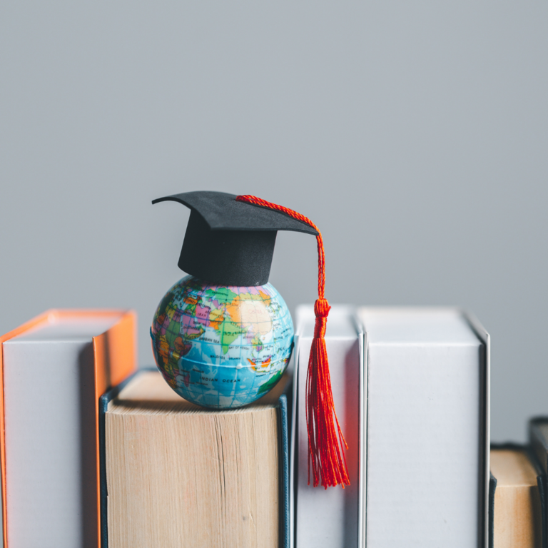 Globe wearing graduation cap sitting over textbooks