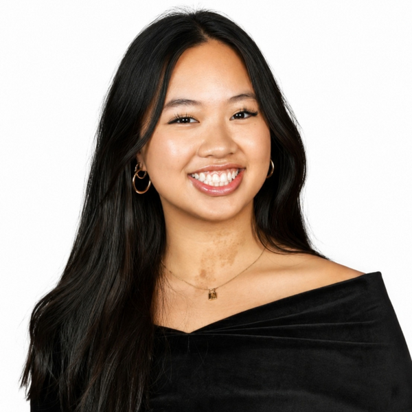 Smiling woman with long dark hair wearing a black off-the-shoulder top, posed against a light background.