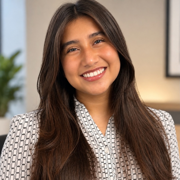 Smiling woman with long dark hair wearing a white patterned top, photographed against a blurred office setting.