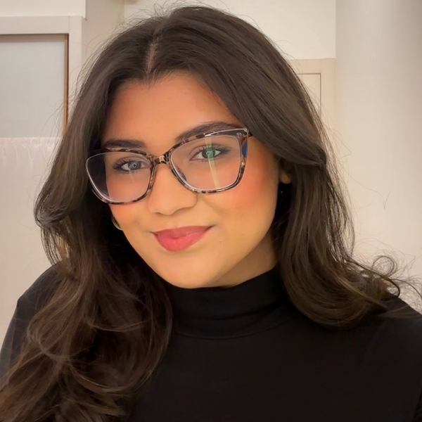 Smiling woman with long dark hair wearing glasses and a black top, shown in a close-up portrait.